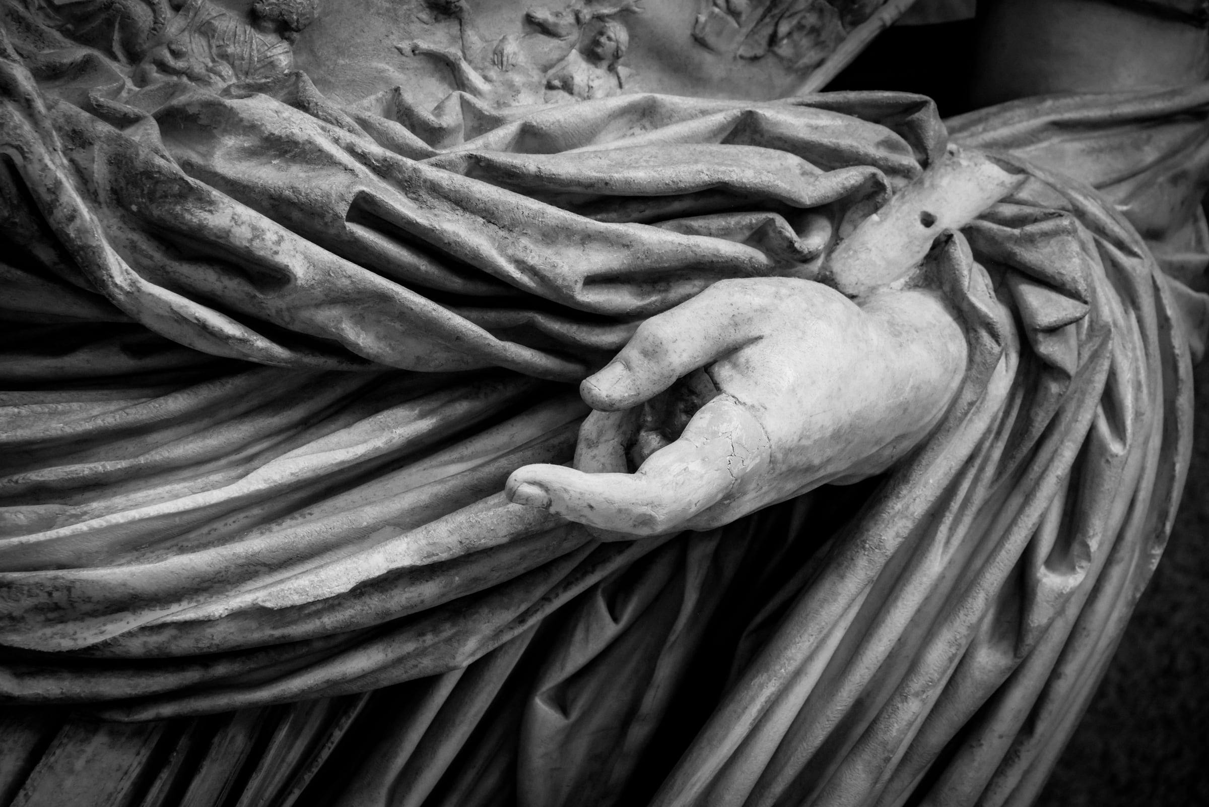 Schwarz-Weiß-Nahaufnahme einer römischen Marmorstatue: Hand und Faltenwurf einer Toga